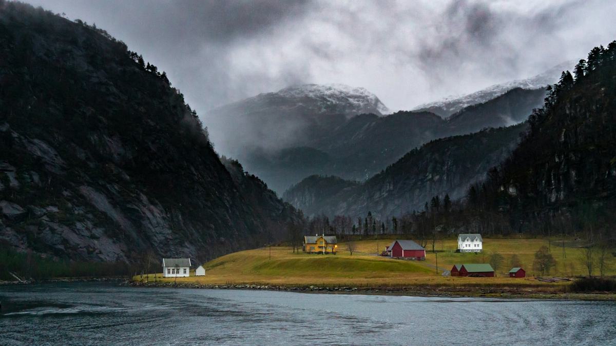 Misty fjord with a red cabin at the water’s edge, Norway